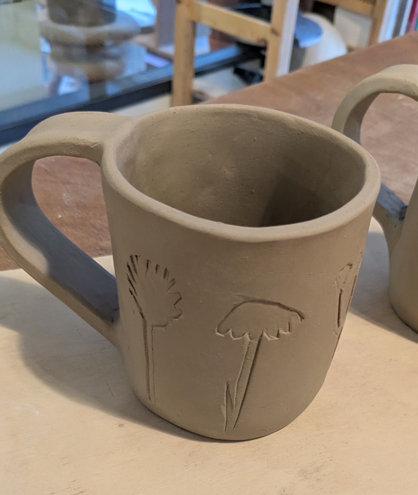 Mug en cours de façonnage à l'atelier, terre crue marquée d'empreintes de graminées